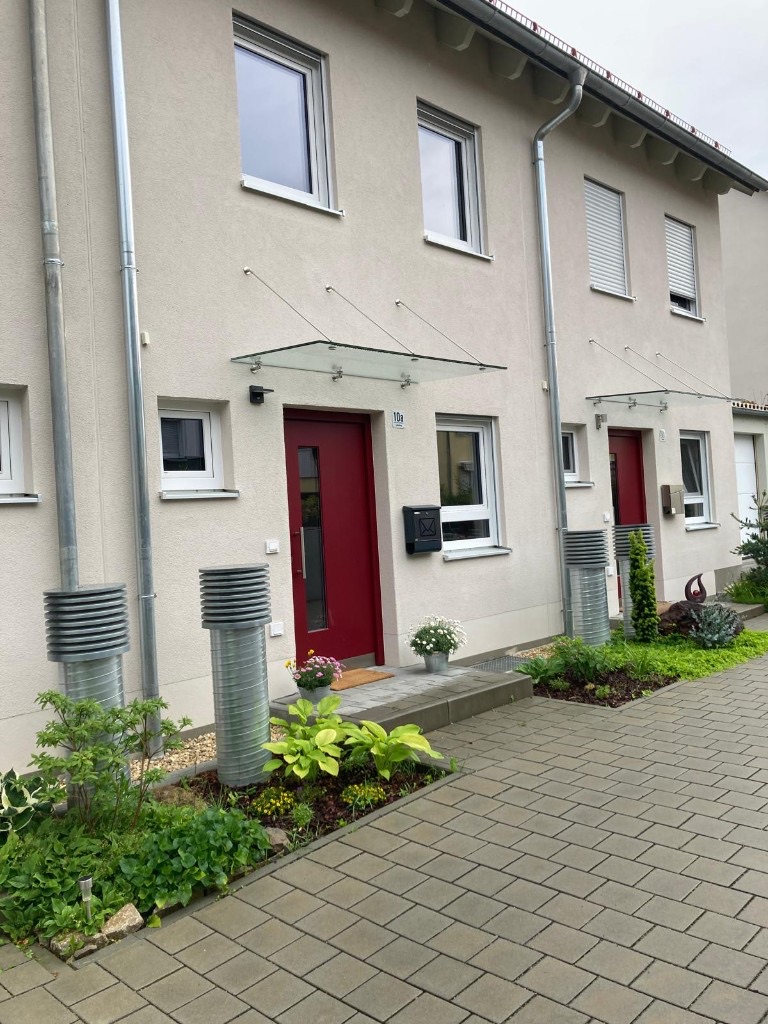 Reihenmittelhaus mit roter Haustür, Glasvordach und gepflegtem Eingangsbereich
